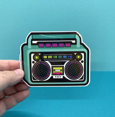 Hand holding teal Boom Box Die Cut Sticker on a blue background