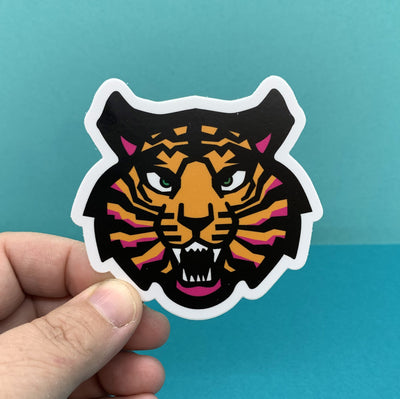Hand holding a tiger die cut sticker by Tomato Tomato Creative on a blue background