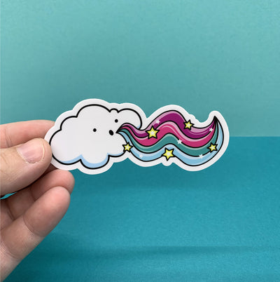 Hand holding a die cut sticker of a cloud by Tomato Tomato Creative on a blue background