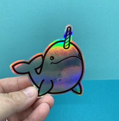 Hand holding holographic narwhal sticker on a blue background